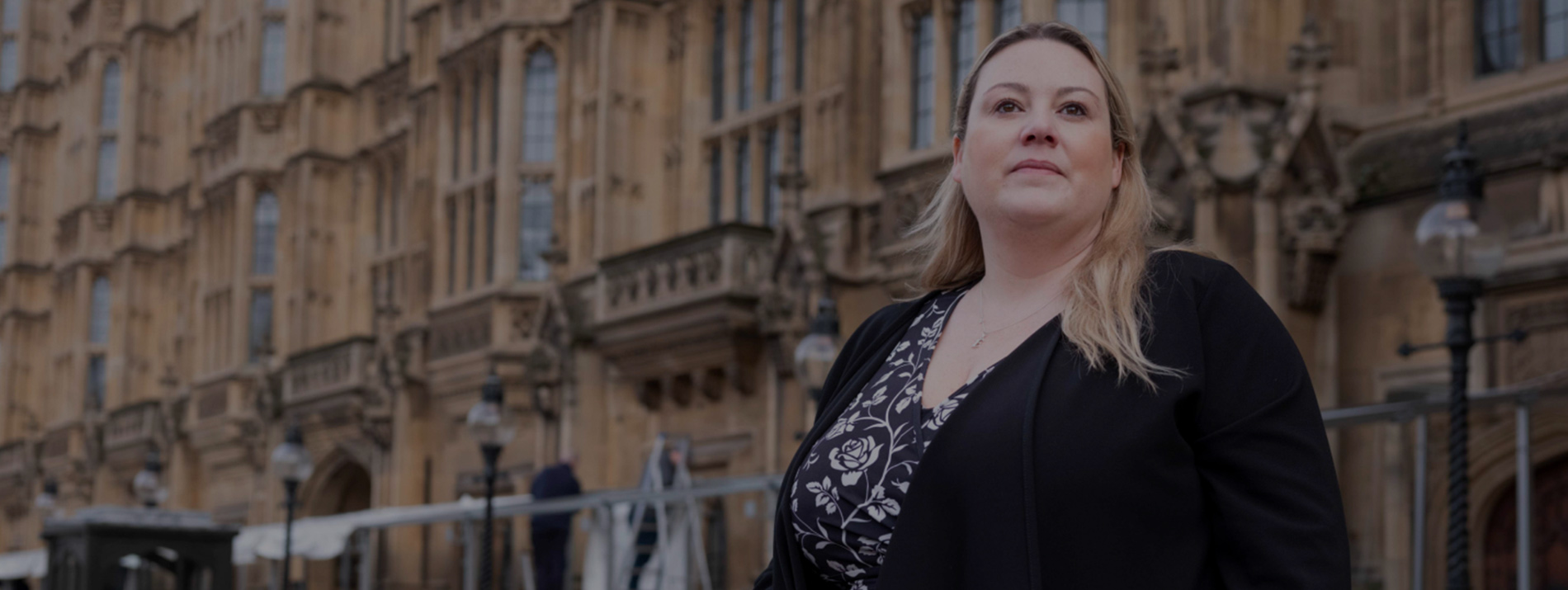 Man in red shirt with headset on, leaning smilingly up against a window