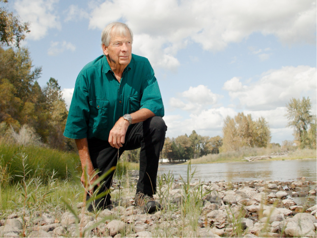 Mann kniet auf dem Boden in der Natur neben einem Fluss